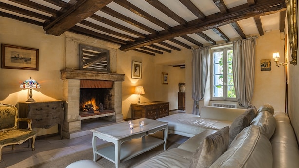 A cozy living room with a fireplace, a sofa, a coffee table, and a lamp. - 18th century stone house in the heart of the D-Day landing beaches  (Ver-Sur-Mer)