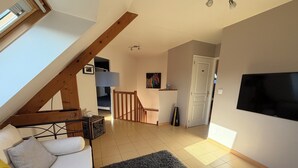 A loft-style room with a sloped ceiling, a sofa, a TV, and a staircase leading to another room.