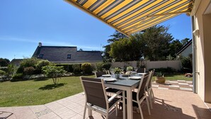 An outdoor patio with a table set for dining, surrounded by chairs, under a striped awning.