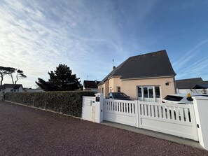 A residential building with a gated driveway, a carport, and a well-maintained hedge.