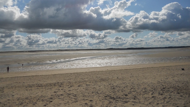 A beach with a wide sandy shore and a clear sky with scattered clouds.