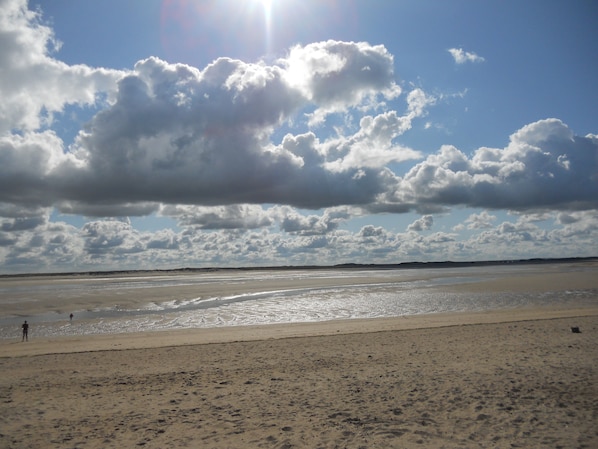 Ein Strand mit weitem Sandufer und einem klaren Himmel mit vereinzelten Wolken.