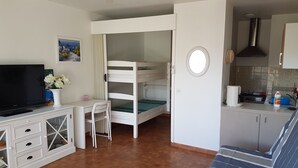 A compact room with a bunk bed, a desk with a chair, a television, and a kitchen area with a sink and stove. - Le Lavandou, La Fossette appt 2/4 pers. beach at 150m. (Le Lavandou)