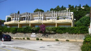 A multi-story hotel with balconies, a parking area, and a stone wall with greenery. - Le Lavandou, La Fossette appt 2/4 pers. beach at 150m. (Le Lavandou)