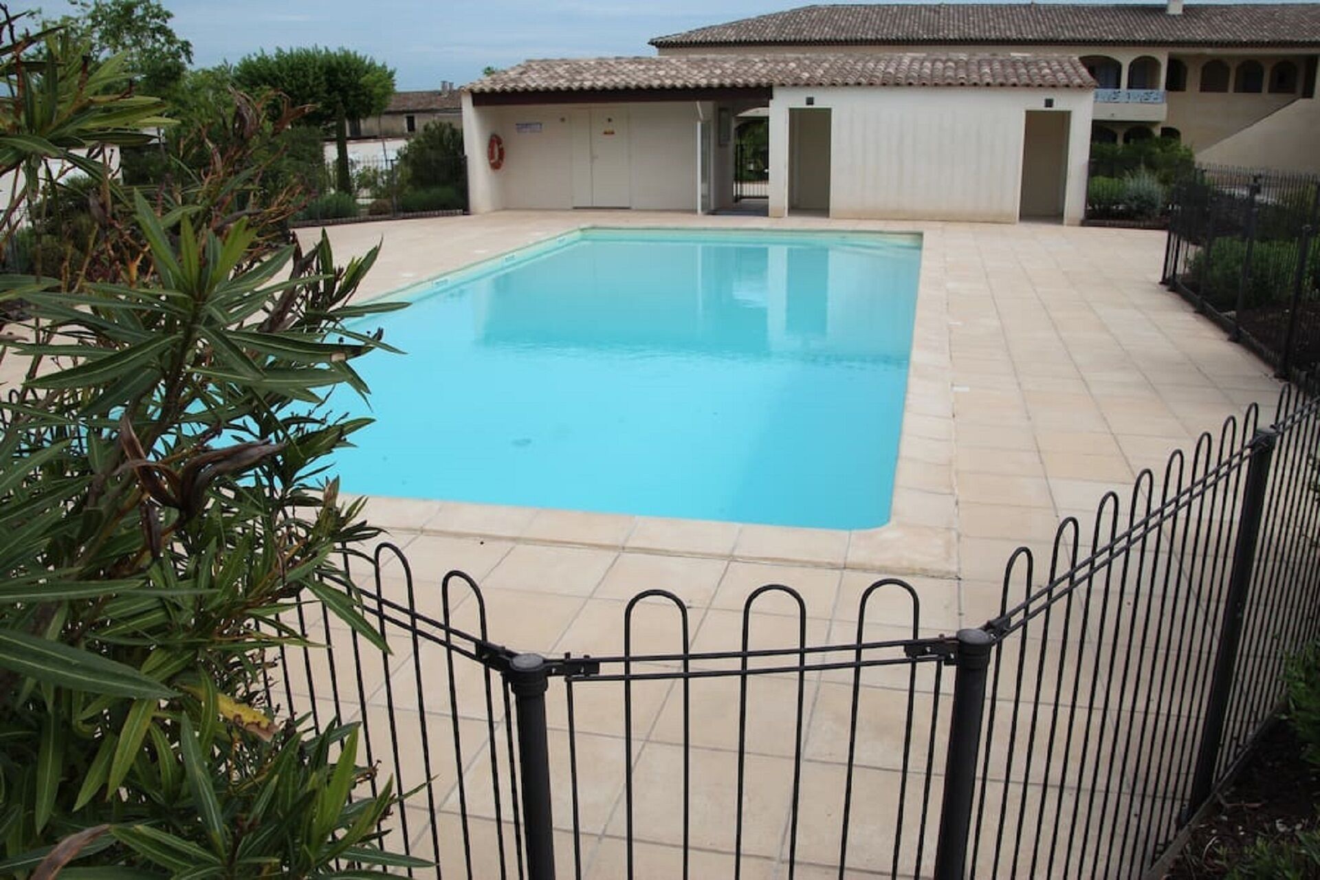 Une piscine rectangulaire avec une plage carrelée, entourée d’une clôture en métal.