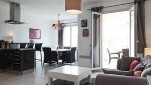 Una sala de estar moderna con una mesa de centro blanca, sillas negras, un sofá gris y un comedor con una mesa y sillas.