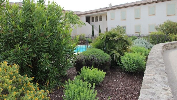 Un patio con piscina, rodeado de diversas plantas y un edificio con ventanales de arco.