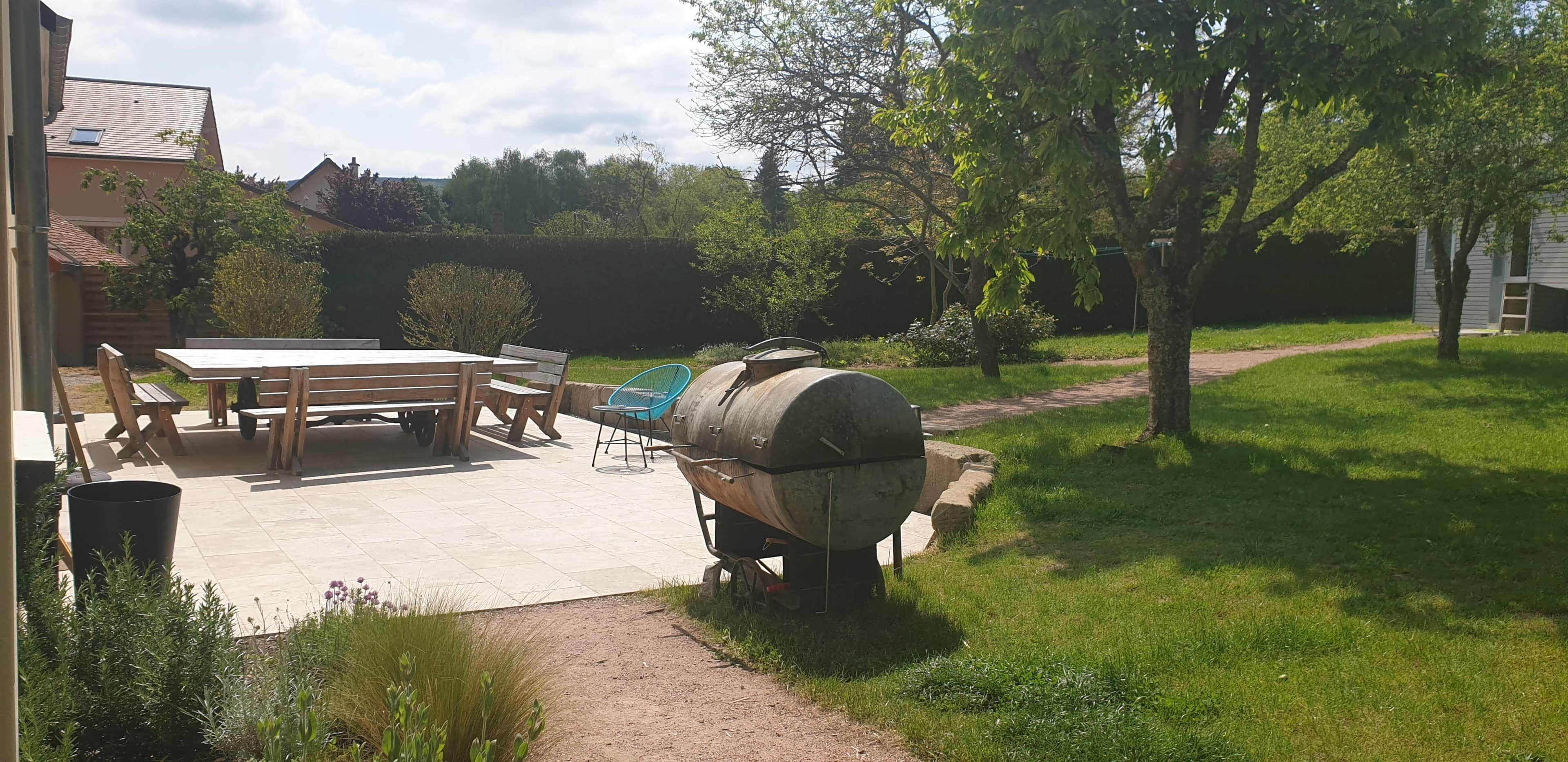 Eine Außenpatio mit Holztisch und -stühlen, einem Grill und einem Gartenweg.