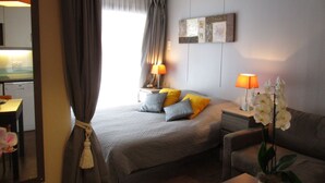 Hotelkamer met een bed, nachtlampjes, een bank, een klein tafeltje, een potorkidee en uitzicht op de keuken.