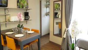Een eetgedeelte met een tafel gedekt voor twee personen, een koffieapparaat en een aan de muur bevestigde televisie.