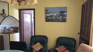 Une pièce comprenant deux fauteuils en cuir vert, une table avec un panier, et un tableau représentant un port de plaisance accroché au mur.