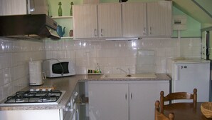Une cuisine de taille réduite, avec des meubles blancs, un four à micro-ondes, une cuisinière à gaz et un réfrigérateur.