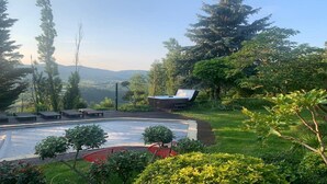 A pool area with lounge chairs and a hot tub, surrounded by lush greenery and trees.