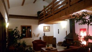A cozy living room with a wooden ceiling, a fireplace, and various plants.