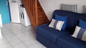 Sala de estar com sofá azul, escada de madeira, máquina de lavar e um quadro na parede.