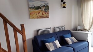 Uma sala de estar moderna com um sofá azul, escada de madeira e um quadro na parede.