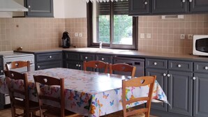 Une cuisine avec des meubles de couleur grise, un pare-feu en carrelage, une fenêtre avec des stores, un four à micro-ondes et une table avec des chaises.