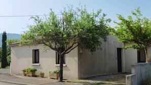 Un petit bâtiment d’un seul étage, à la façade beige, doté d’un petit porche agrémenté de plantes en pot et offrant une vue dégagée sur le paysage environnant.