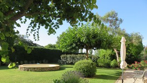 Ein gepflegter Garten mit einem runden Steinbecken, verschiedenen Sträuchern und einem Pergola mit Sonnenschirm.
