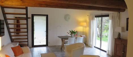 A cozy living room with a wooden ceiling, a sofa, a coffee table, and a dining area with chairs and a table.