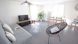 Una sala de estar moderna con sofá, televisión, mesa de comedor, sillas y una planta en maceta.