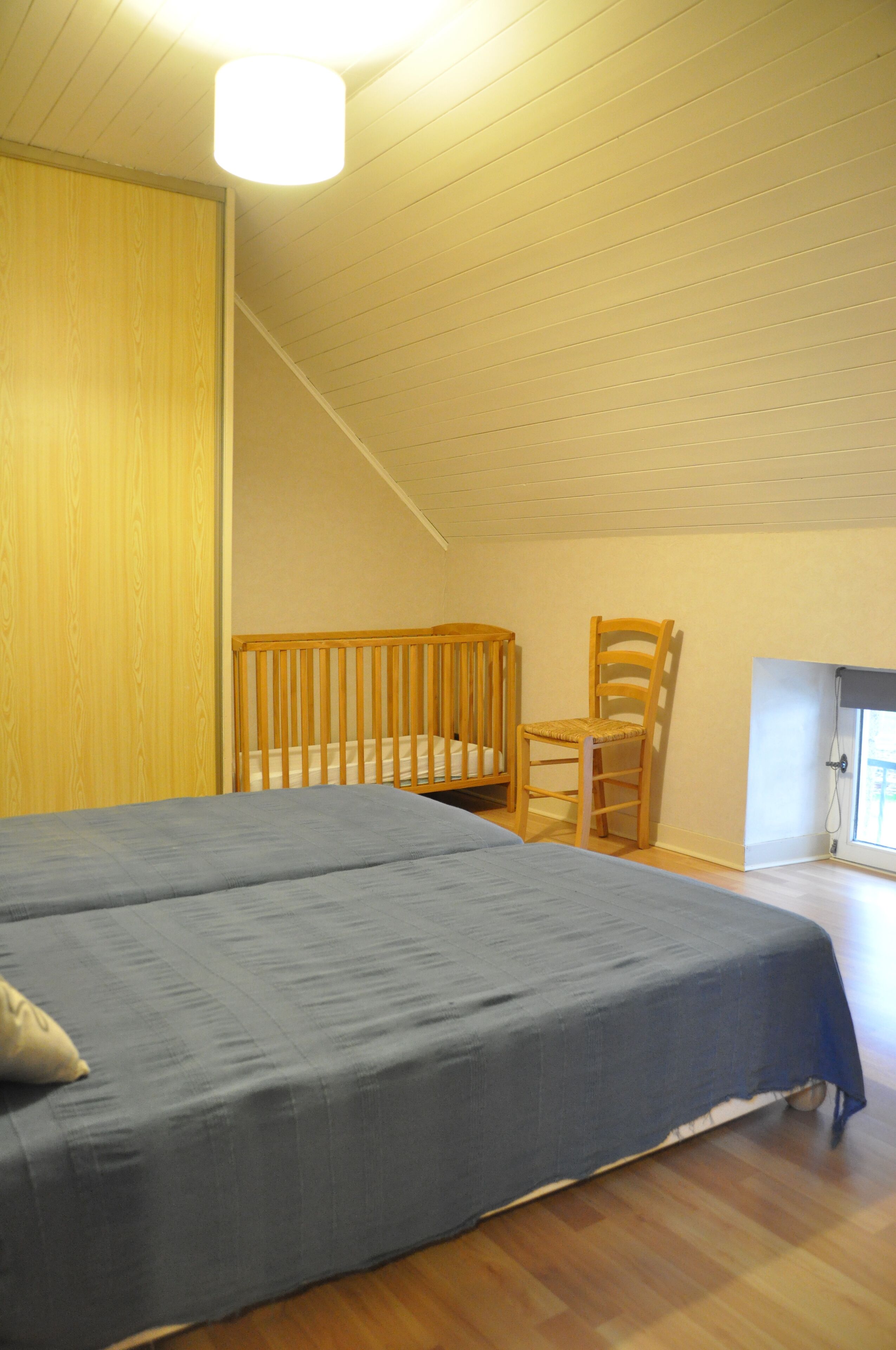 Una habitación con una cama, una cuna de madera, una silla de madera y una ventana con vistas.