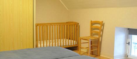 Una habitación con una cama, una cuna de madera, una silla de madera y una ventana con vistas.