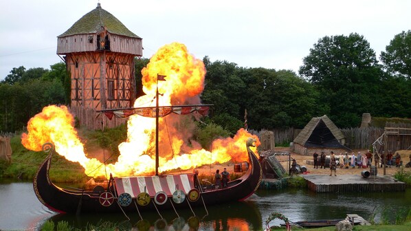 A Viking ship on fire with people on board, set against a backdrop of a wooden tower and a small dock area. - Private, quiet accommodation in architect-designed house with pool, spa, private garden (Soucelles)