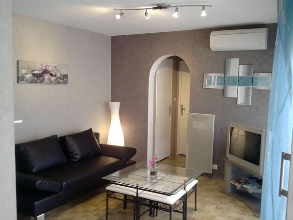 Ein modernes Wohnzimmer mit einem dunkelgrauen Ledersofa, einem Couchtisch mit Glasplatte, einer Stehlampe und einem Flachbildfernseher.