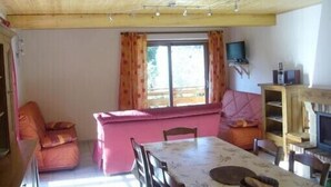 A cozy living room with a wooden ceiling, a pink sofa, a dining table with chairs, and a fireplace. - Cottage in the heart of the Vercors national park, sleeps 11, fully equipped (Saint-Martin-En-Vercors)