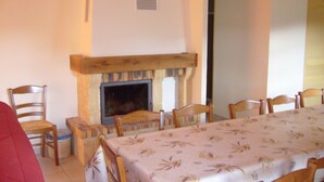 A dining area with a fireplace, wooden chairs, and a table covered with a floral tablecloth. - Cottage in the heart of the Vercors national park, sleeps 11, fully equipped (Saint-Martin-En-Vercors)
