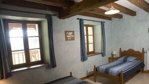 A bedroom with two wooden beds, a window with curtains, a small bedside table with a lamp, and a framed picture on the wall. - Renovated 120 square metre gîte in old farmhouse (La Pesse)