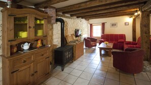 A cozy living room with a stone wall, wooden furniture, a fireplace, and a television. - Renovated 120 square metre gîte in old farmhouse (La Pesse)