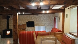 A cozy living room with a stone wall, wooden beams, a fireplace, a sofa, and a table. - Renovated 120 square metre gîte in old farmhouse (La Pesse)