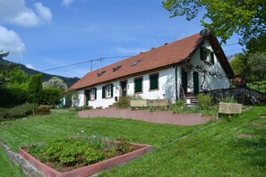 Une maison blanche avec un toit rouge, des volets verts et un jardin.
