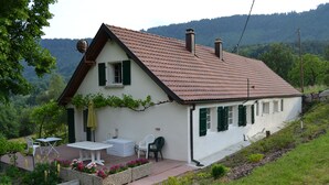 A two-story house with a sloped roof, a patio with outdoor furniture, and a garden with flowers.