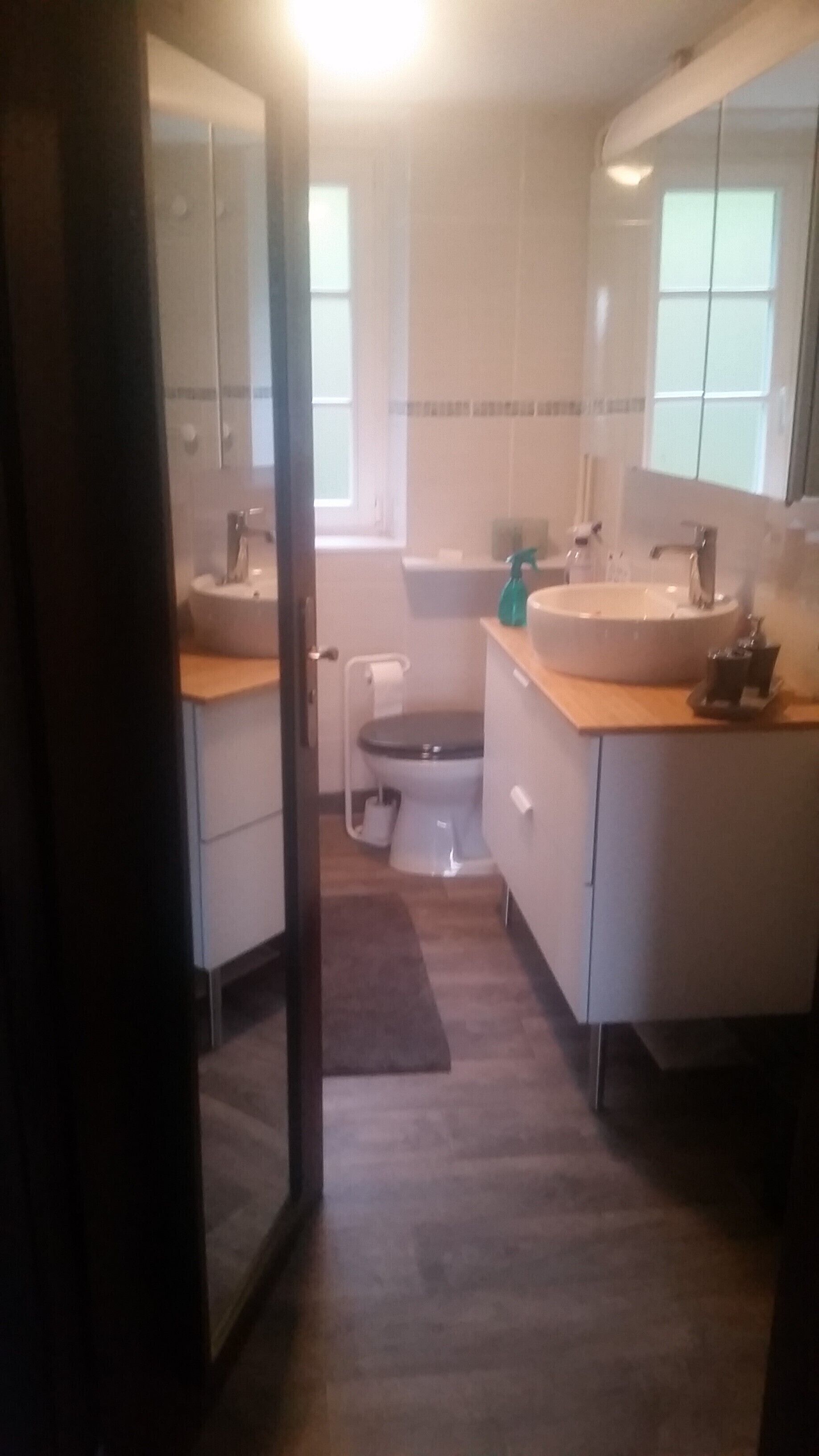 A bathroom with a toilet, sink, and mirror. There is a window providing natural light.