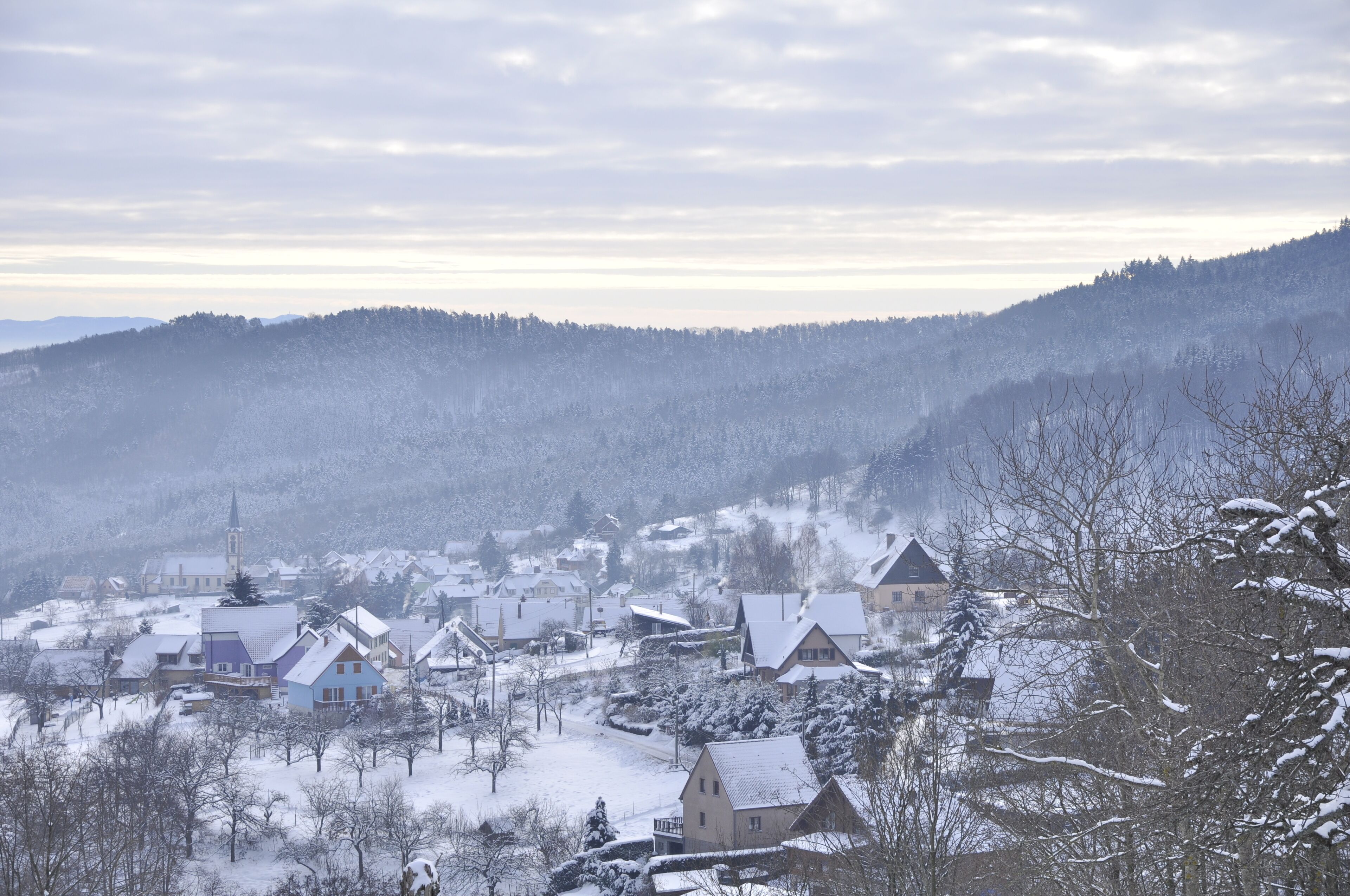 A snow-covered village with traditional houses and a church, surrounded by hills.