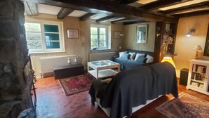 A cozy living room with a sofa, coffee table, and a fireplace. There are windows and a stone wall visible.