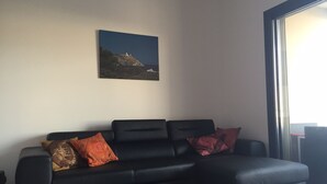 En sort lædersofa med to røde og en orange pude foran en hvid væg, med et indrammet landskabsmaleri over sofaen.