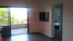 Et moderne værelse med et fladskærms-tv ophængt på væggen, en balkon med et bord, og en seng i det tilstødende rum.