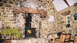 A stone-walled room with a fireplace, a wooden bench, and a chair. - Holiday cottage near the sea that can accommodate 11 people (Argol)