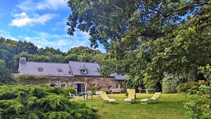 A stone house with a sloped roof, surrounded by a well-maintained lawn and various trees. - Holiday cottage near the sea that can accommodate 11 people (Argol)