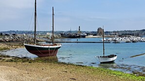 A harbor with boats, a stone building, and a lighthouse in the background. - Holiday cottage near the sea that can accommodate 11 people (Argol)
