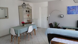 A dining area with a table and chairs, a bookshelf, a radiator, a door, a plant, and a TV on a stand. - Appt House 72M² 2/4 persons 50m SEA BEACH (Châtelaillon-Plage)