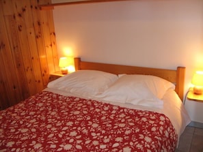 A bed with white linens and a red floral bedspread, two bedside lamps, and wooden paneling on the wall.