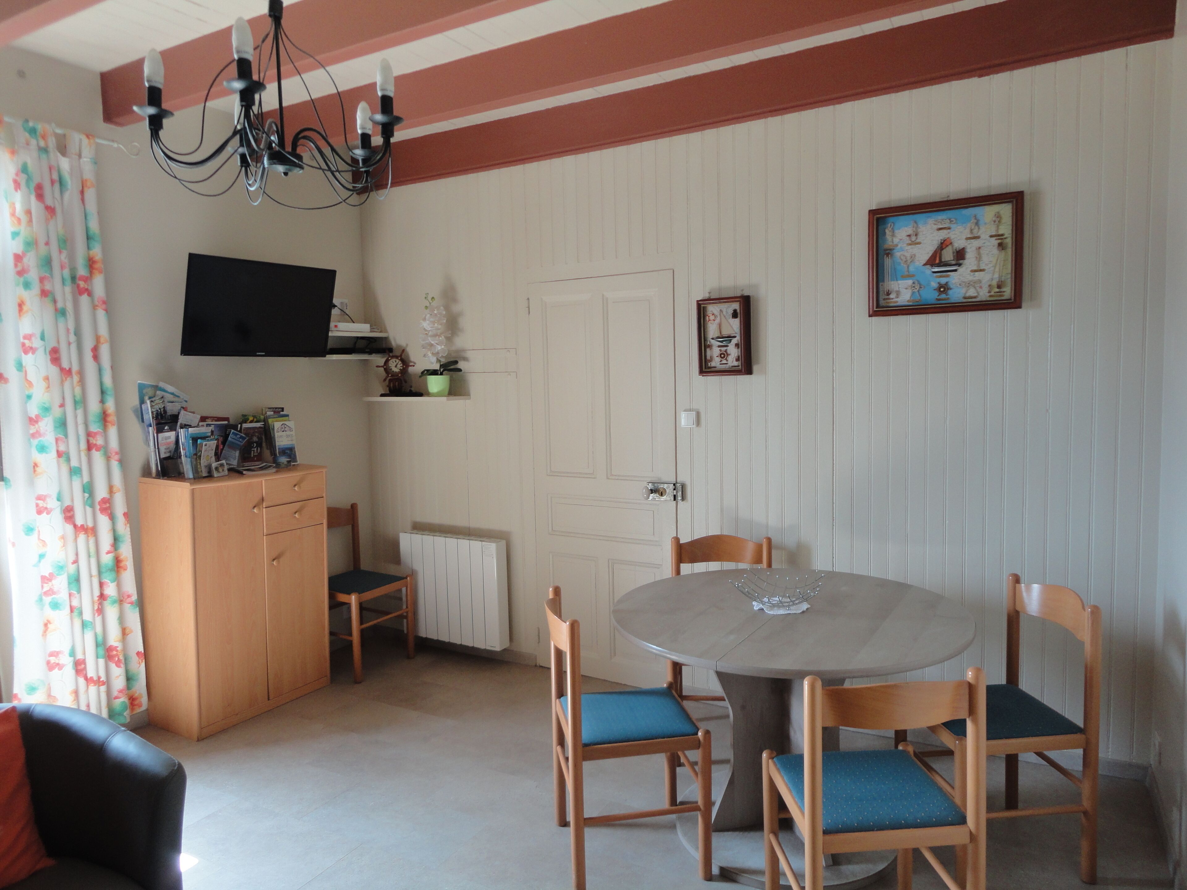 Ein Essbereich mit einem runden Tisch, vier Stühlen, einer Holzkommode, einem an der Wand befestigten Fernseher und einer Tür mit einem kleinen Bilderrahmen.
