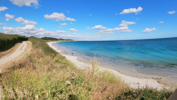 A coastal road leading to a beach with clear blue waters and a few people in the distance. - Exceptional sea and island view. A haven for nature in a protected site (Névez)