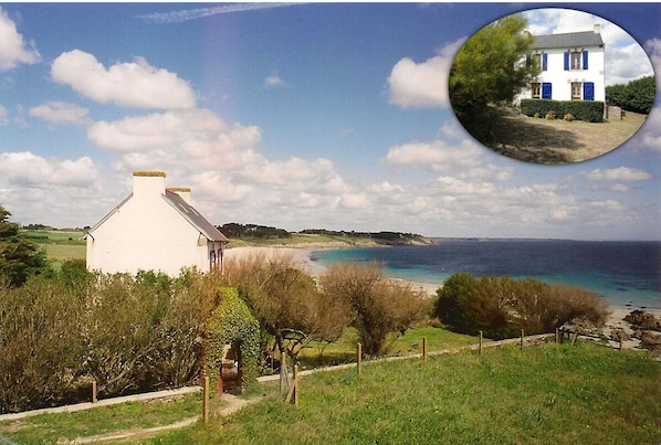 A coastal house with a white exterior, a visible garden, and a view of the sea.