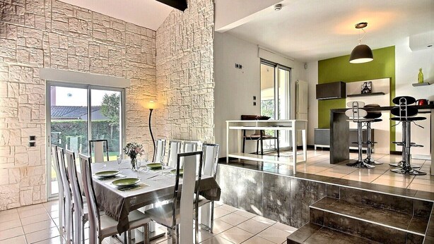 A modern dining area with a stone wall, a dining table set for four, and a view of the outdoors. - Beautiful Villa with Large Heated Pool and Sea Water, 5 km from the Beach (Portiragnes)